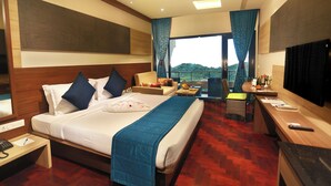 A hotel room with a large bed, a desk, a TV, and a balcony with a view.