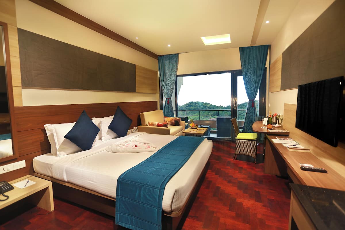 A hotel room with a large bed, a desk, a TV, and a balcony with a view.