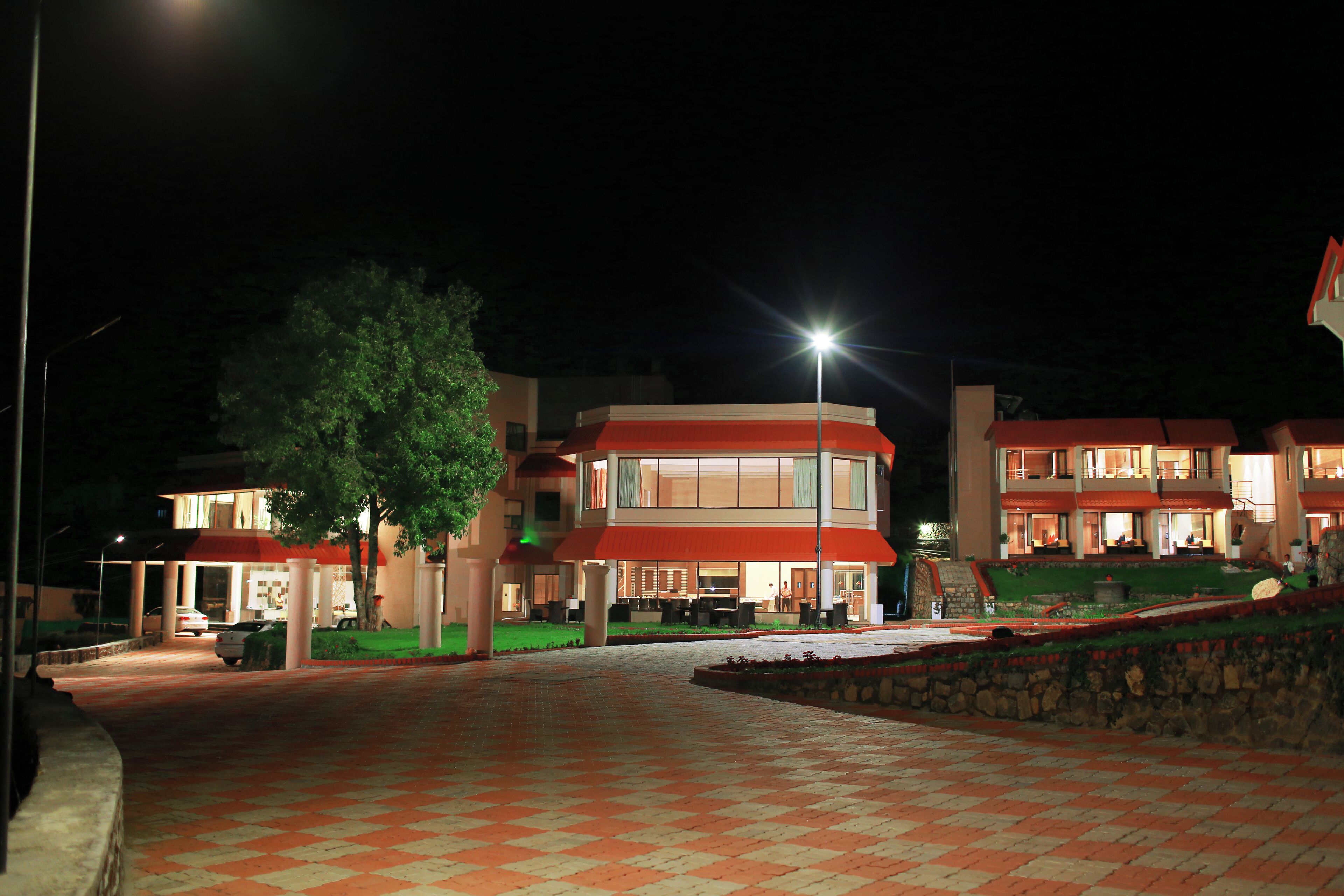 Un hotel con techo rojo, varios pisos y un camino pavimentado que lleva a la entrada.