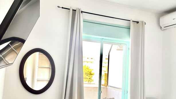 Un dormitorio con cama, una silla, un espejo redondo y vistas a un espacio exterior con una silla y una mesa.