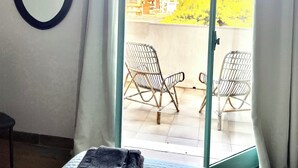 Una habitación con cama, un espejo redondo y un balcón con dos sillas de mimbre.