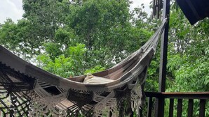 Un hamac suspendu entre des poutres en bois sur une terrasse en bois, entouré d’une végétation luxuriante.
