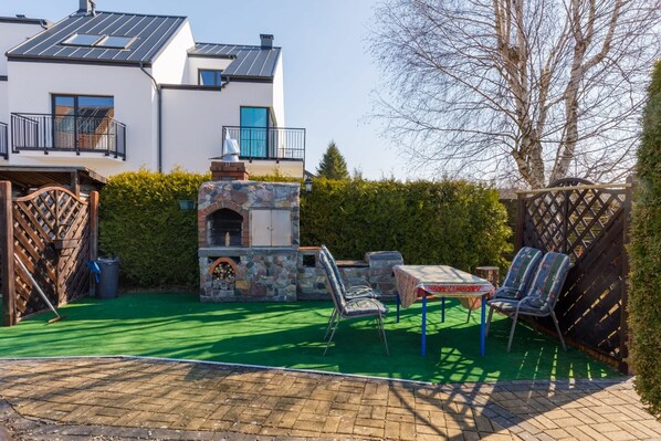 A modern house with a stone barbecue area, outdoor seating, and a view of the neighboring building.