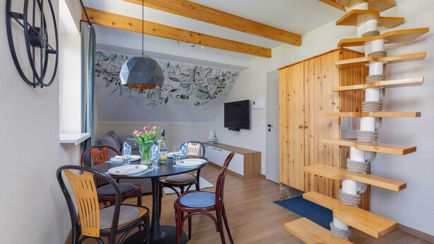 A dining area with a round table, chairs, a wall-mounted TV, and a wooden staircase.