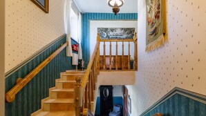 A staircase with wooden railings, a blue wall with a patterned wallpaper, and a painting above the landing.