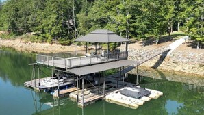 A docked boat with a covered deck and lounge area, surrounded by trees and a calm lake. - Stunning 4-bedroom house with amazing outdoor space and dock in Double Springs. (Double Springs)