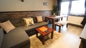 A living room with a sofa, a coffee table, a small table with a plant, and a window with curtains. - Apartment Haus Tauern Am See  (Heiterwang)