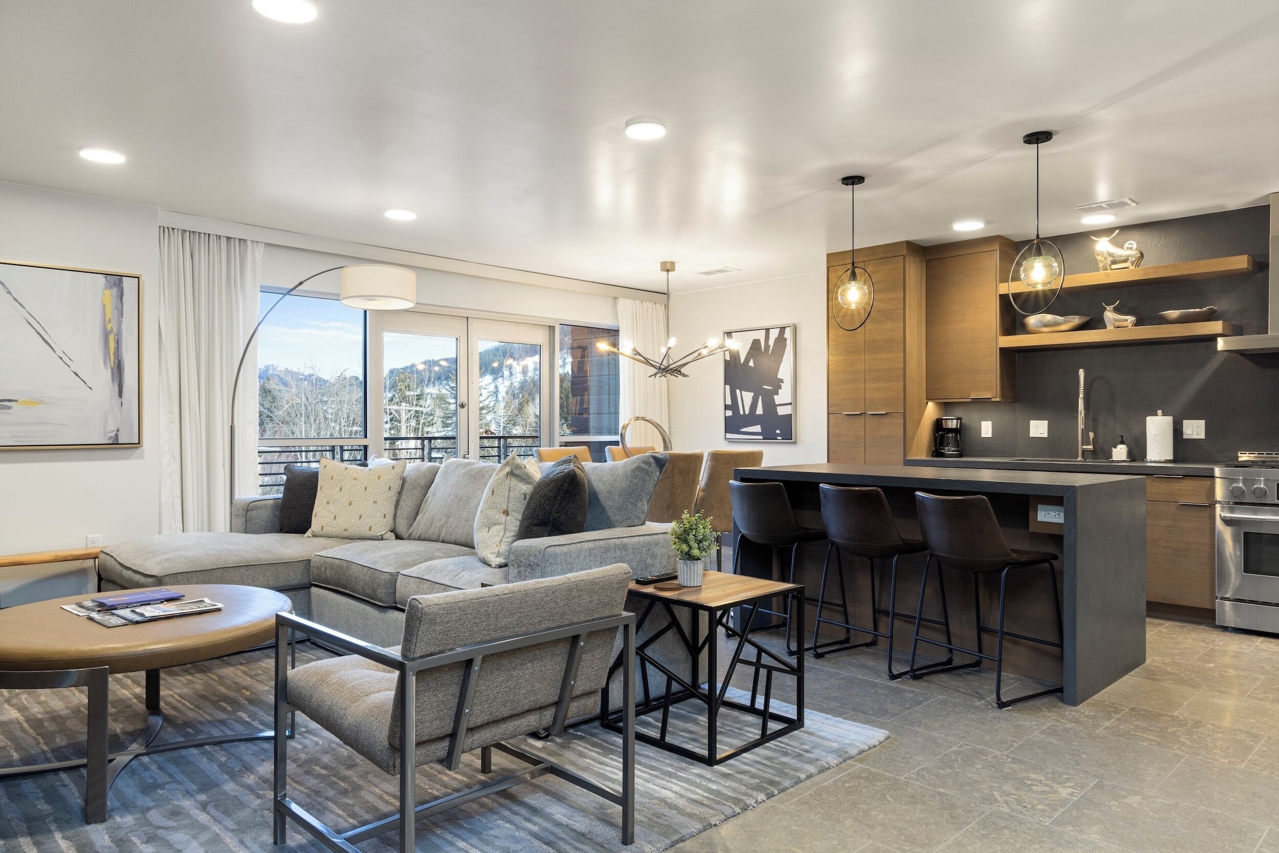 A modern living room with a sectional sofa, a small coffee table, and a kitchen area with bar stools and a built-in island.