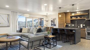 A modern living room with a sectional sofa, a small coffee table, and a kitchen area with bar stools and a built-in island.