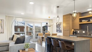 Una cocina moderna con una isla central, taburetes de bar y un área de comedor con sofá y mesa de centro.