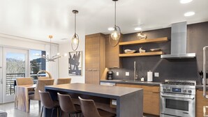 Una cocina moderna con una isla central, taburetes de bar, electrodomésticos de acero inoxidable y armarios de madera.