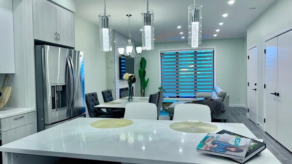 Una cocina moderna con una isla grande, electrodomésticos de acero inoxidable e iluminación colgante.