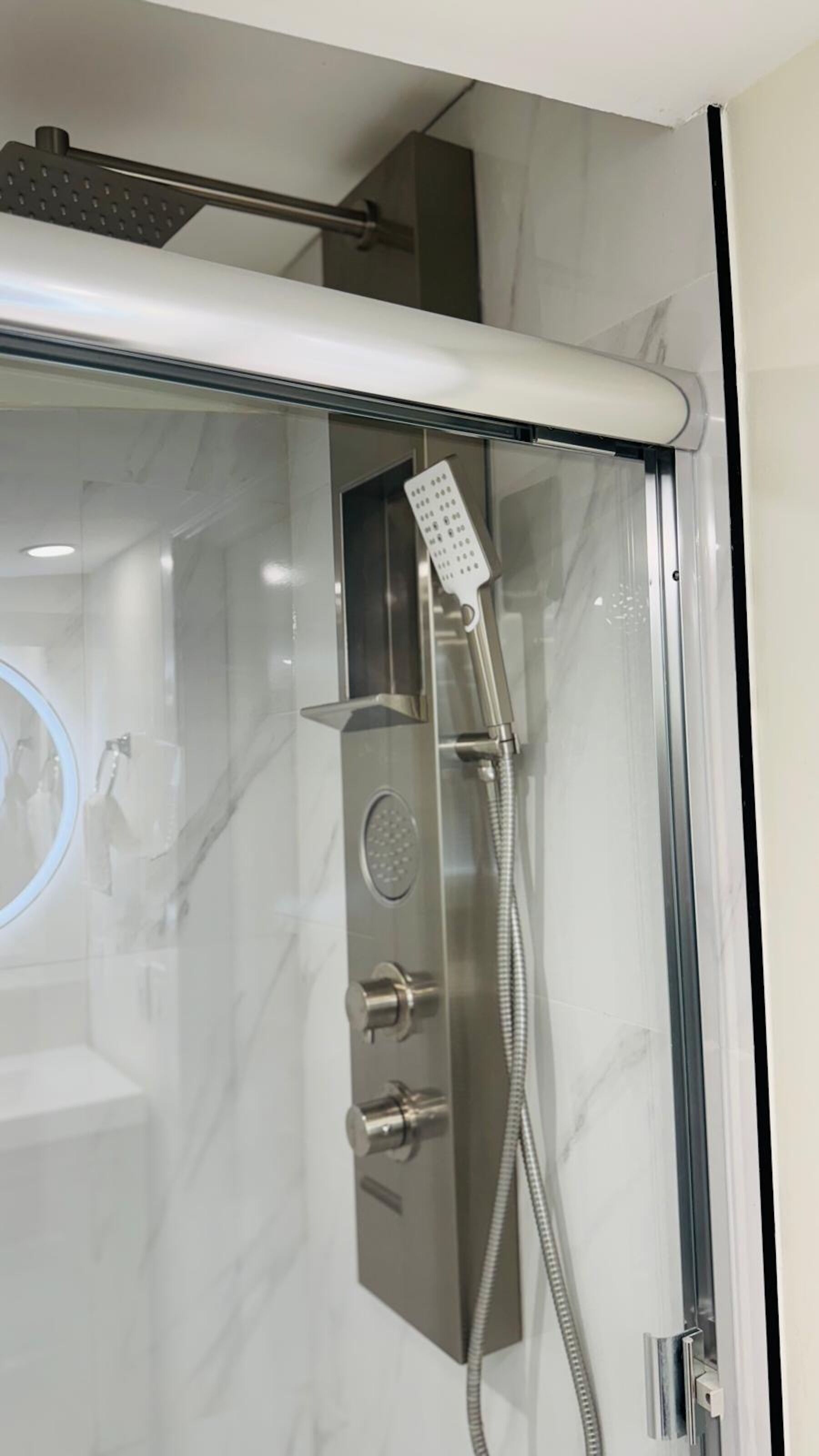 A modern shower with a handheld showerhead, a wall-mounted control panel, and a glass-enclosed shower area.