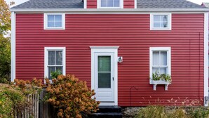 Ein rotes, zweistöckiges Haus mit weißer Tür, Fenstern und einer kleinen Veranda.