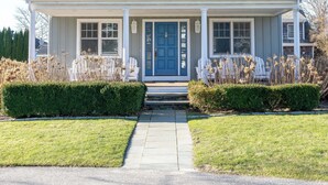 A two-story house with a front porch, a blue door, and a small garden with dried plants. - Spectacular View from Rooftop Deck | Sleeps 12 (Middletown)