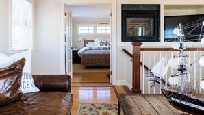 A living room with a brown leather sofa, a wooden coffee table, and a large ship model. There is a bed with a floral bedspread in the background. - Spectacular View from Rooftop Deck | Sleeps 12 (Middletown)