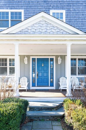 A house with a blue door, white porch columns, and two white Adirondack chairs.