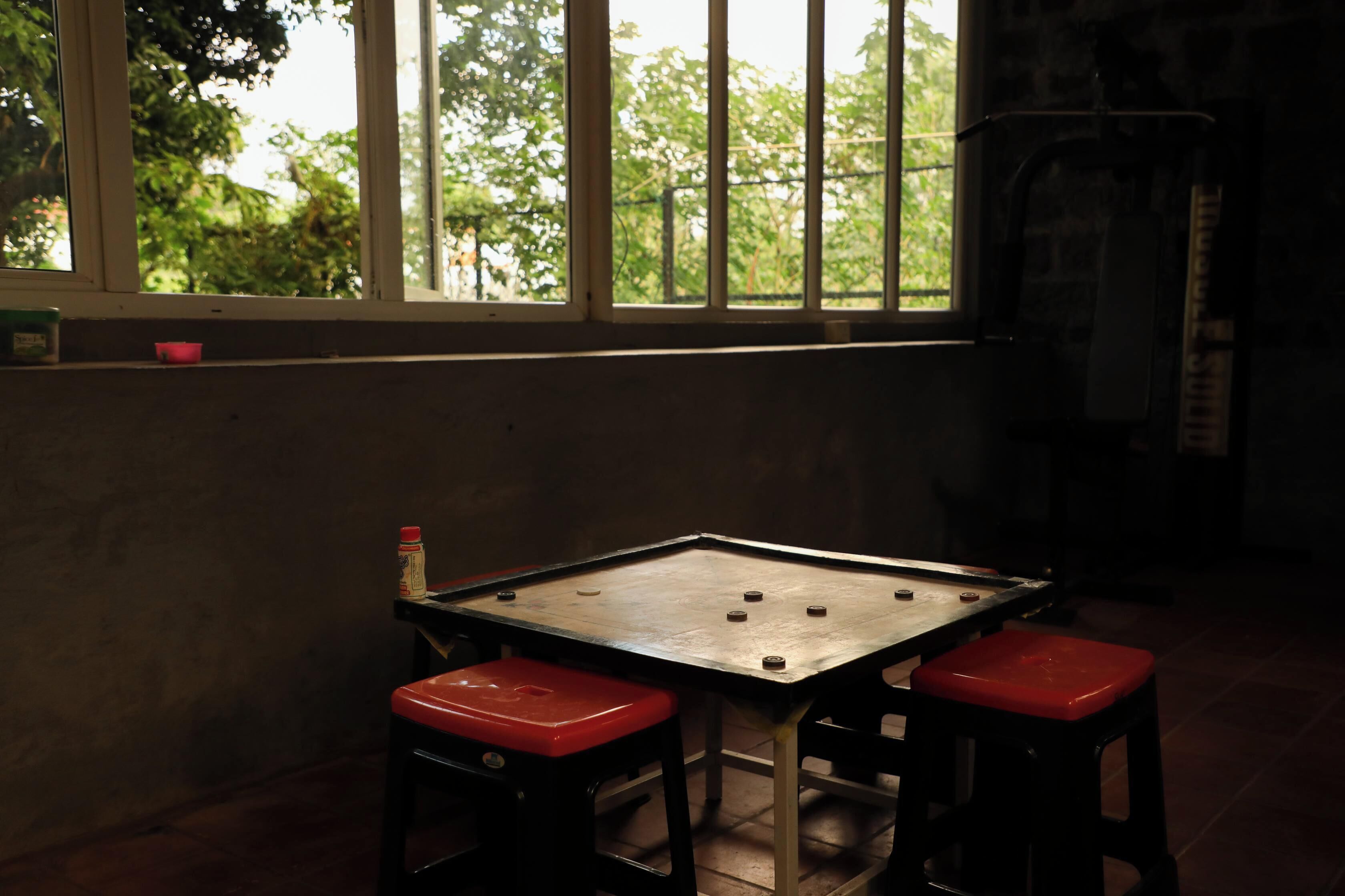 A room with a table and two stools, a window with a view of trees, and a wall-mounted heater.