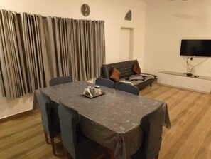 Un comedor con una mesa preparada para cuatro personas, un sofá, un televisor y cortinas.