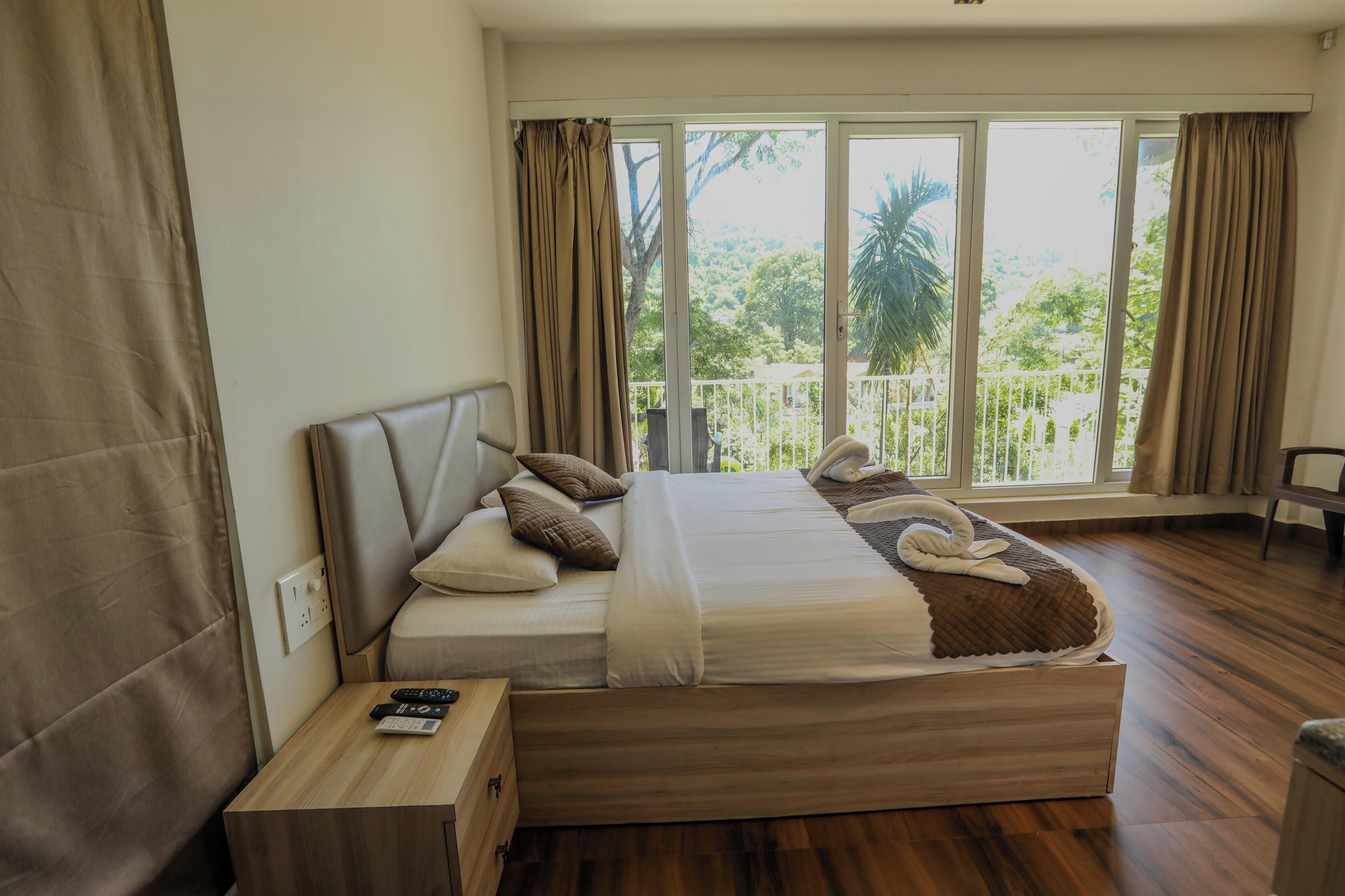 A bedroom with a large bed, a nightstand, and a view of greenery through the window.