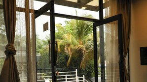 Une chambre avec un lit, une vue sur un balcon agrémenté d’un palmier, et une porte vitrée donnant sur l’extérieur.