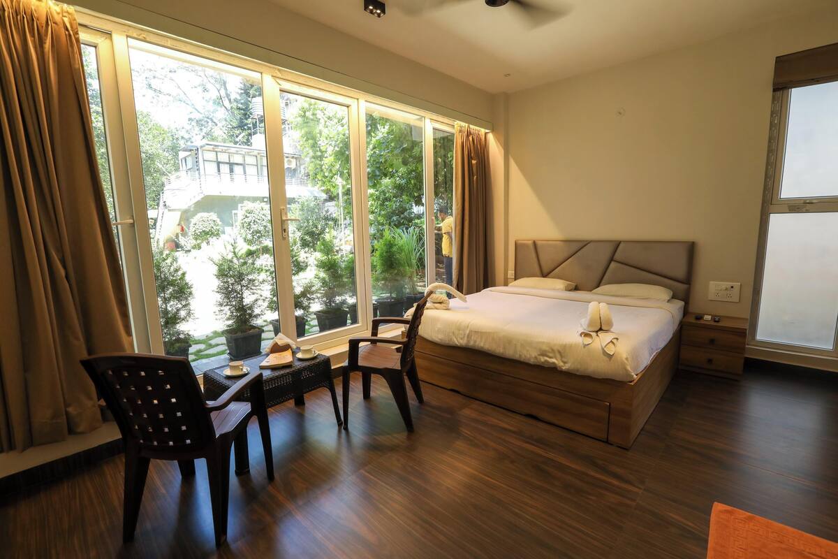 Quarto com uma cama grande, uma escrivaninha com cadeira e vista para um jardim através de amplas janelas.