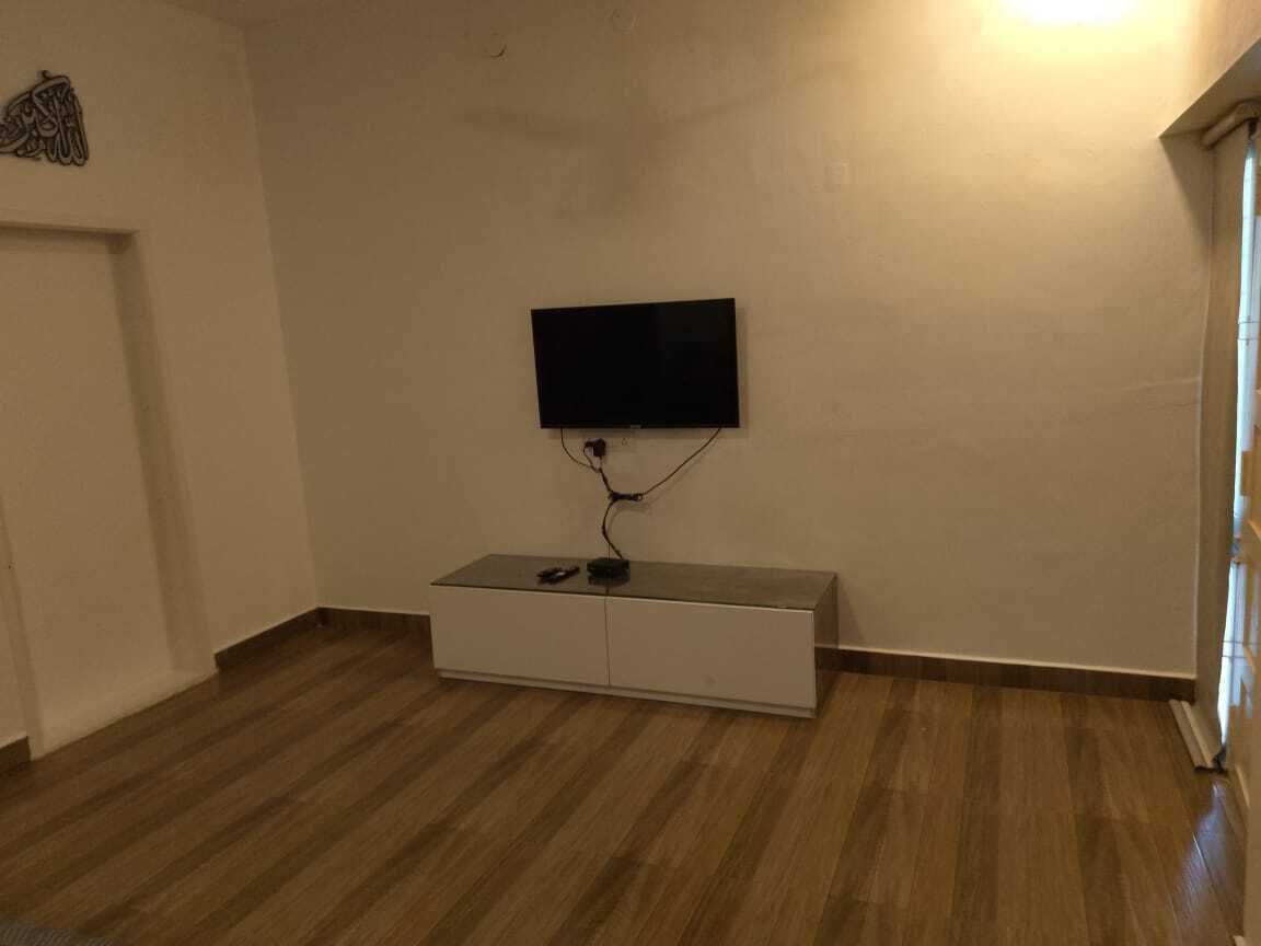 Ett rum med en platt-TV som är monterad på väggen, ett vitt konsolbord och trägolv.