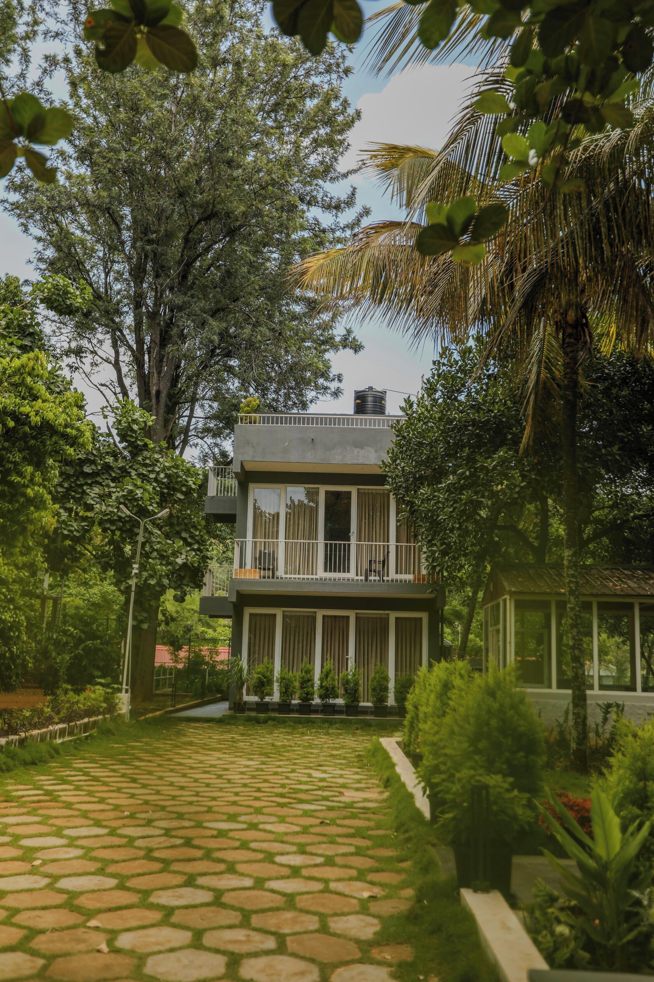 A modern two-story building with a balcony, surrounded by lush greenery and a stone pathway.