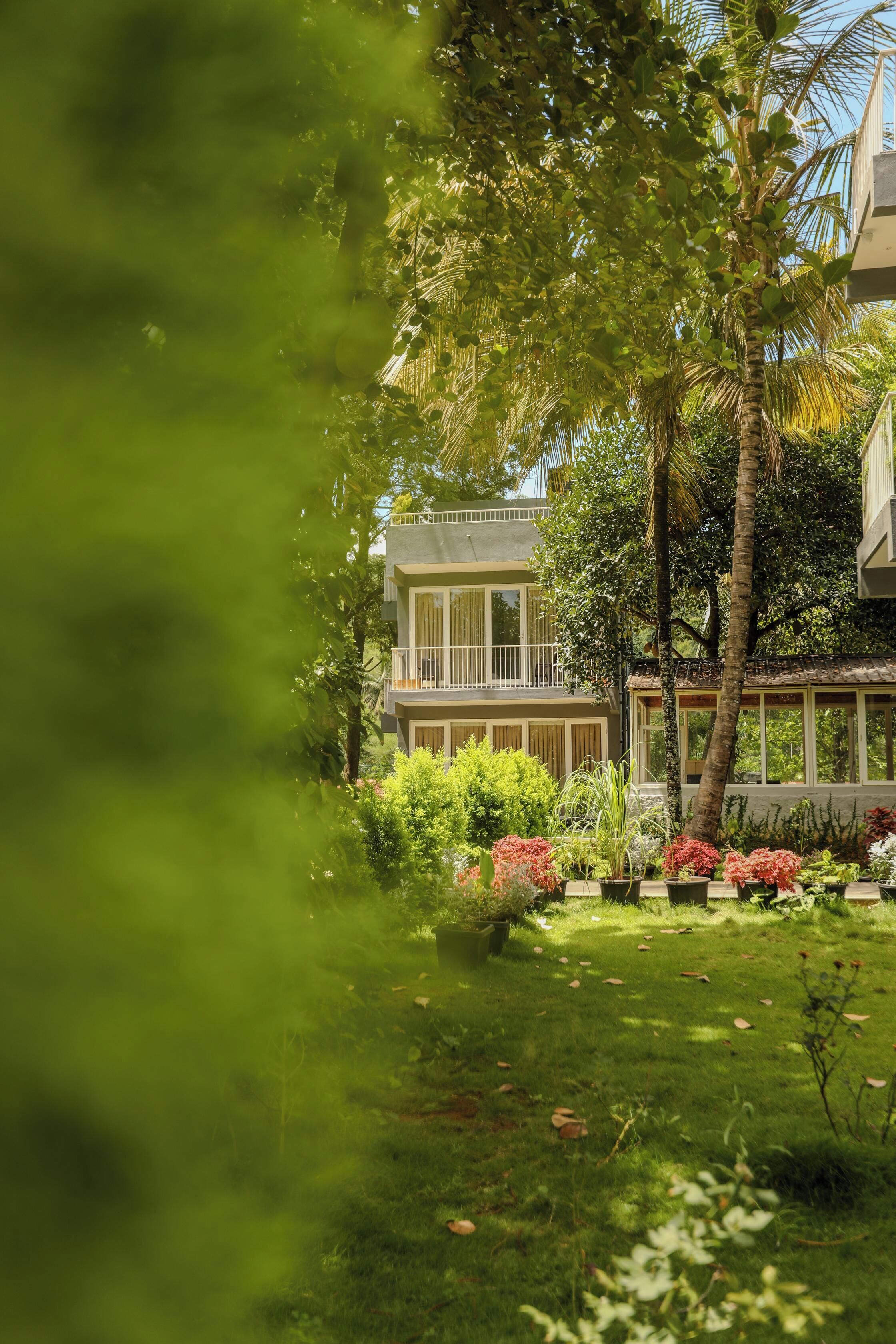 A two-story building with a balcony, surrounded by lush greenery and palm trees.