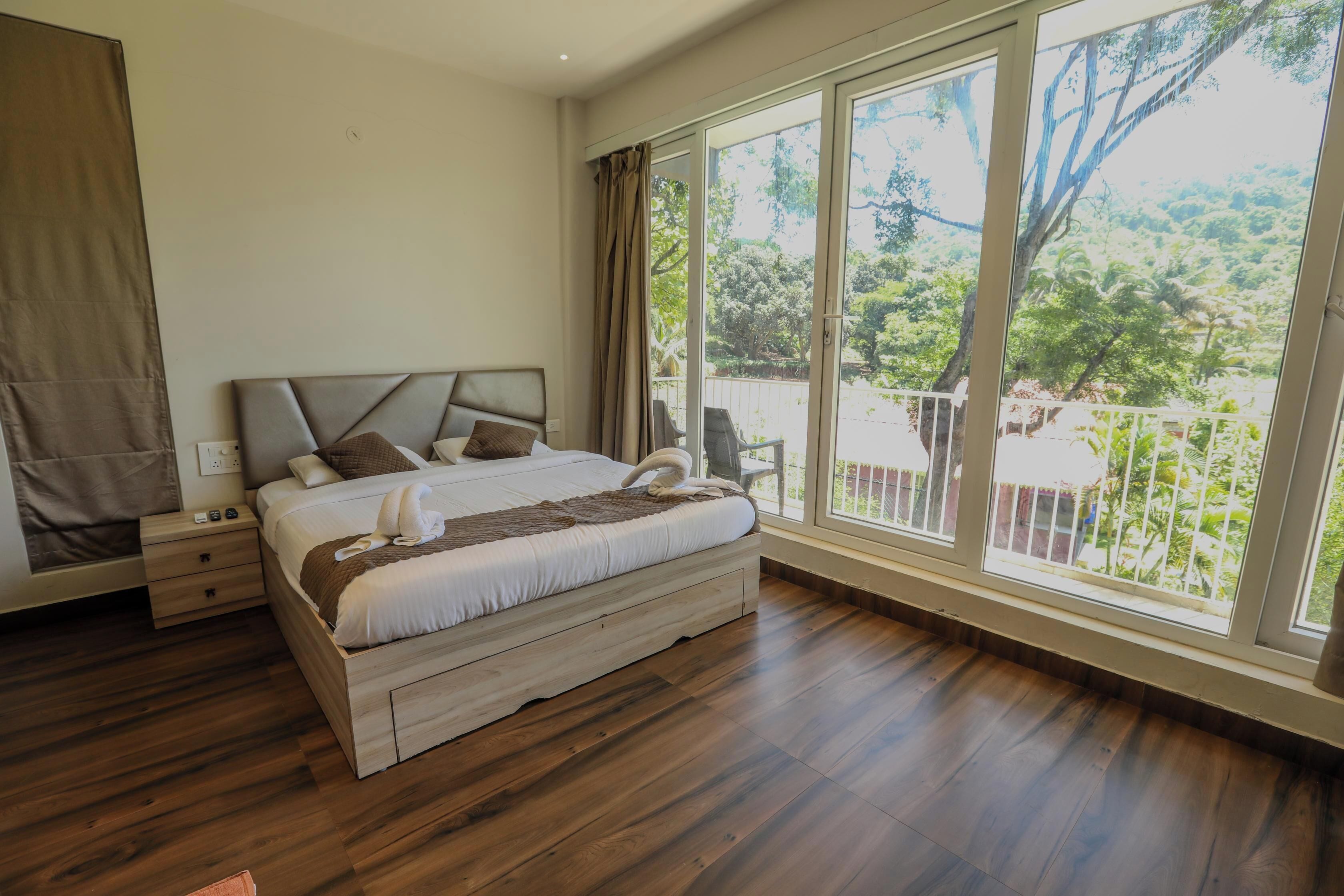 Une chambre dotée d’un grand lit, d’un plancher en bois et d’un balcon offrant une vue sur la verdure.