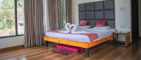 A modern hotel room with a large bed, a headboard, and a view of greenery outside.