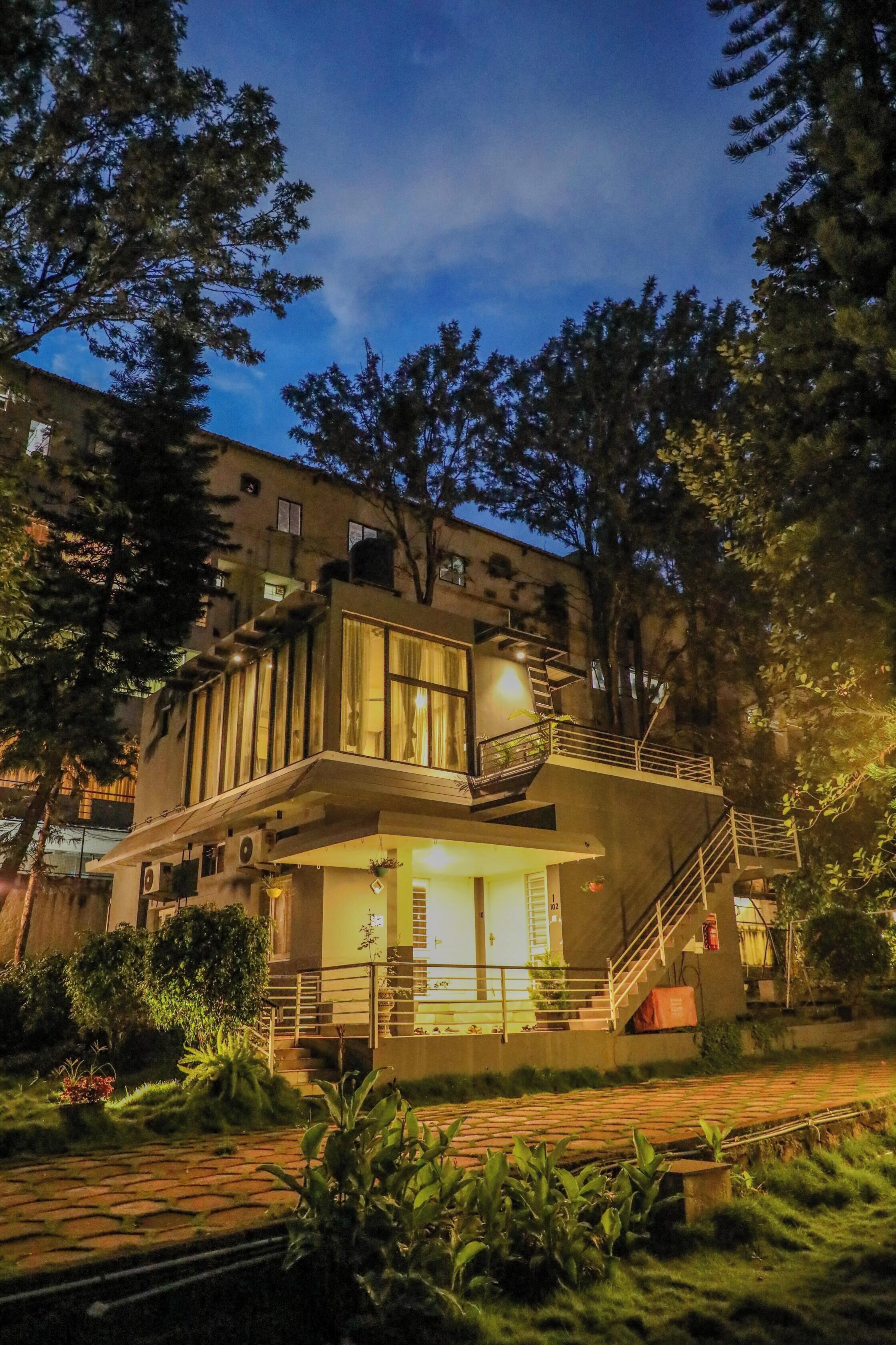 Un edificio moderno de dos pisos con un balcón, una escalera y un pequeño jardín.