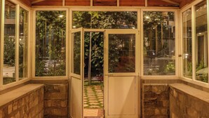 Un patio couvert doté d’un sol carrelé, de poutres en bois au plafond et de portes vitrées donnant sur un jardin.