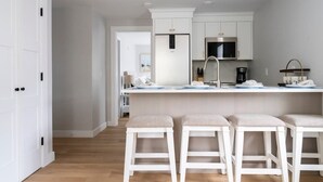 A modern kitchen with white cabinetry, a central island with stools, a microwave, and a coffee machine.