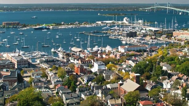 A coastal town with a marina, buildings, and a bridge in the background.