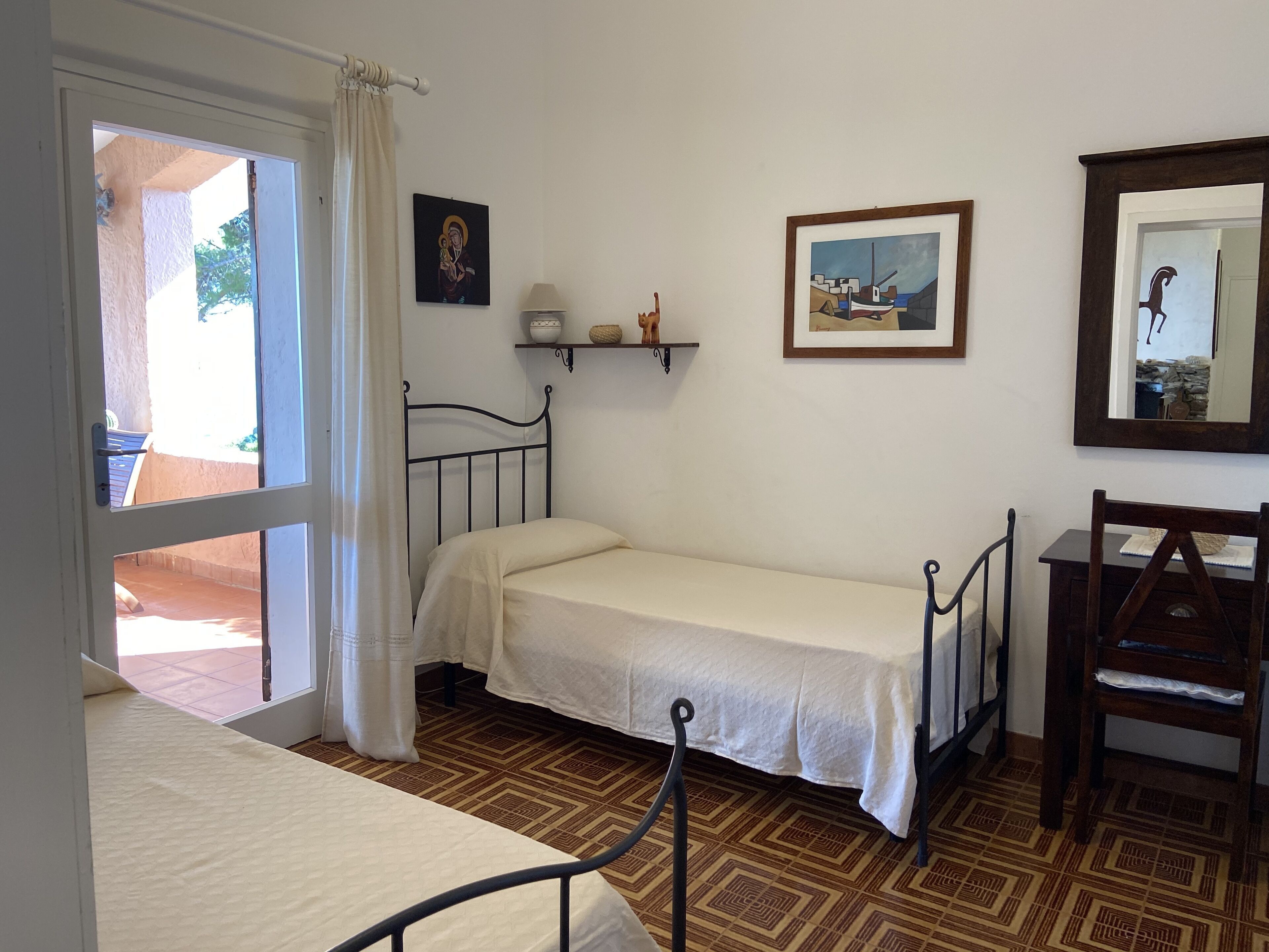 A small, simple room with a bed, a chair, a table, and a window with a curtain.