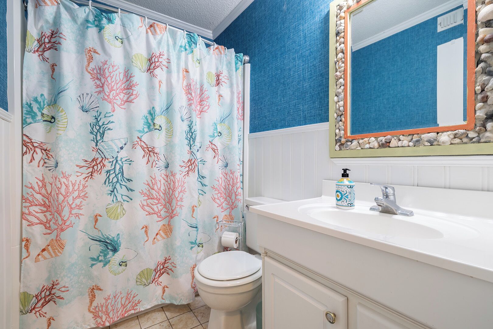 A bathroom with a blue wall, a white sink, a toilet, and a shower curtain with a coral reef pattern.