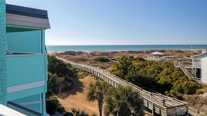A coastal view with a wooden boardwalk leading to a beach area, a blue building, and a clear sky. - SeaSpray 350, Oceanview Condo in Atlantic Beach, NC! (Atlantic Beach)
