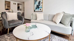 Een moderne woonkamer met een grijze fauteuil, een witte bank en een ronde salontafel met een bloevas.