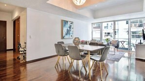Een moderne eetruimte met een grote tafel, grijze stoelen en een kroonluchter.