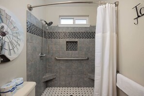 Bathroom features a shower with a curved glass door and handrail, surrounded by large and small tiles.