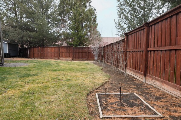 Enjoy the serene atmosphere of this backyard with a lush lawn and a raised garden bed.