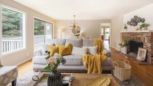 A living room with a sofa, fireplace, and large windows overlooking a deck. - Serene 3b2b Home, Family-Friendly, Backyard & A/C (Redmond)