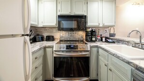 Cocina compacta con alacenas blancas, horno de acero inoxidable, microondas y pileta.