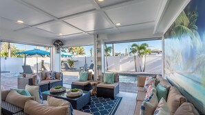 A sunlit indoor patio with wicker furniture, a pool view, and a large mural. - 🌊Private Pool-Great for Large Groups-6BR Coral Cove🌊 (Fort Myers Beach)