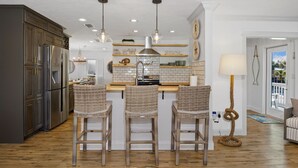 A kitchen with a central island, bar stools, a refrigerator, and pendant lighting. - 🌊🏖️ Coral Cove B | Screened Porch + Pool | Steps to Beach + Times Square (Fort Myers Beach)