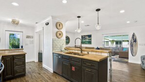 A modern kitchen with dark cabinetry, a wooden countertop, and a central island with a sink. - 🌊🏖️ Coral Cove B | Screened Porch + Pool | Steps to Beach + Times Square (Fort Myers Beach)