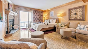 A hotel room with a bed, a sofa, a fireplace, and a balcony. - Cozy Studio with Fireplace, King Bed, A/C (Ellicottville)