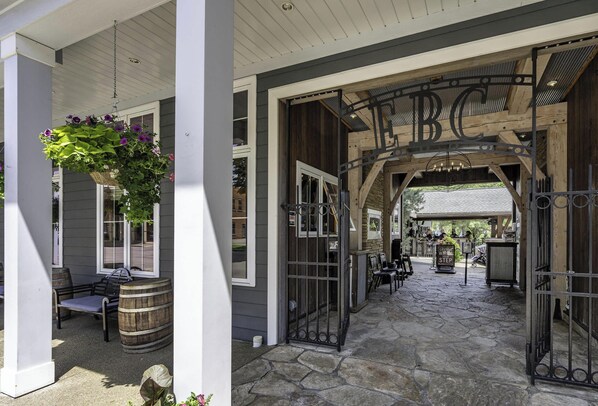A covered outdoor area with a wooden bench, a hanging flower basket, and a stone pathway leading to a gate with 'BC' above it.
