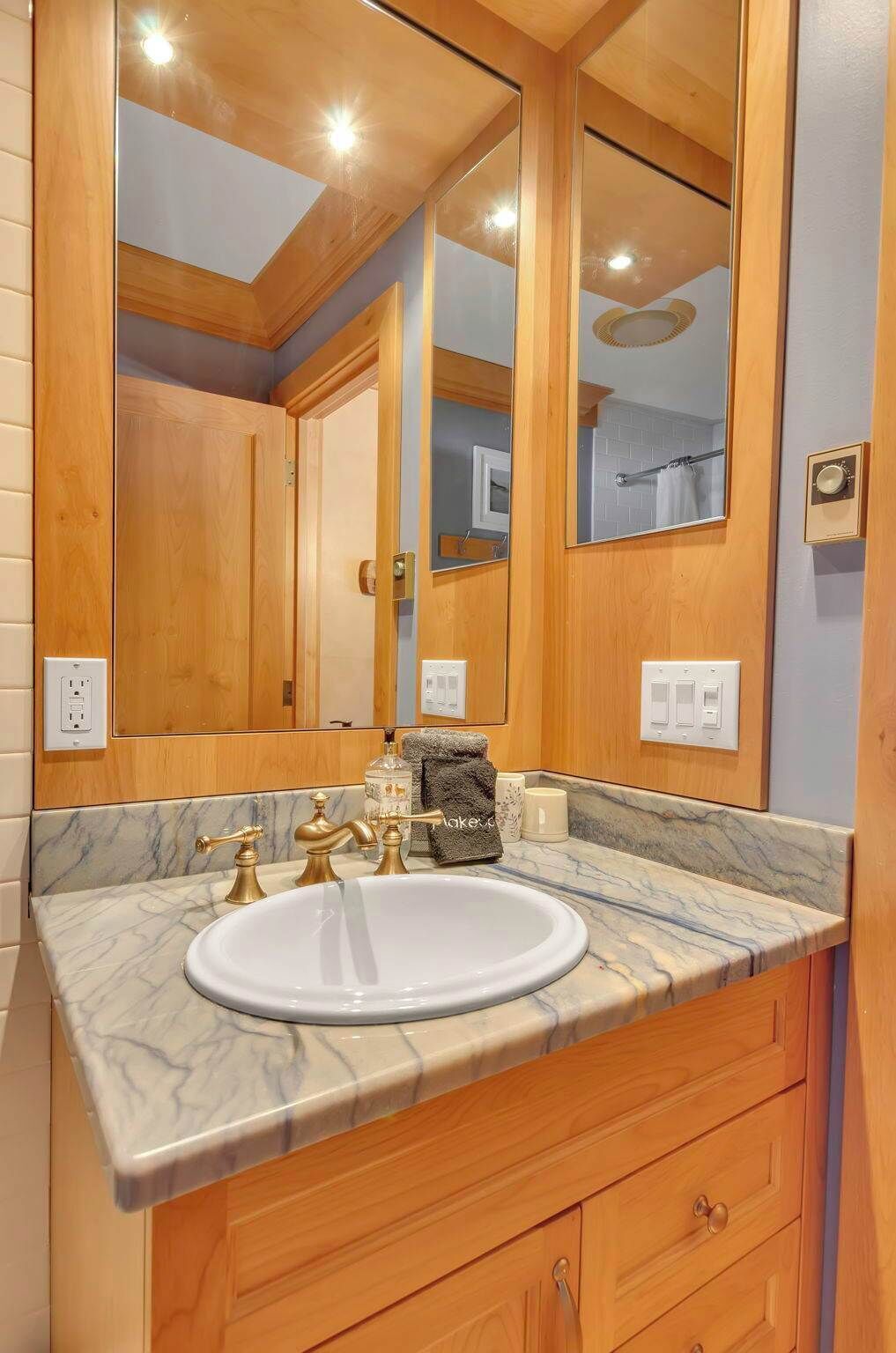 A bathroom with a marble sink, wooden vanity, and a large mirror.